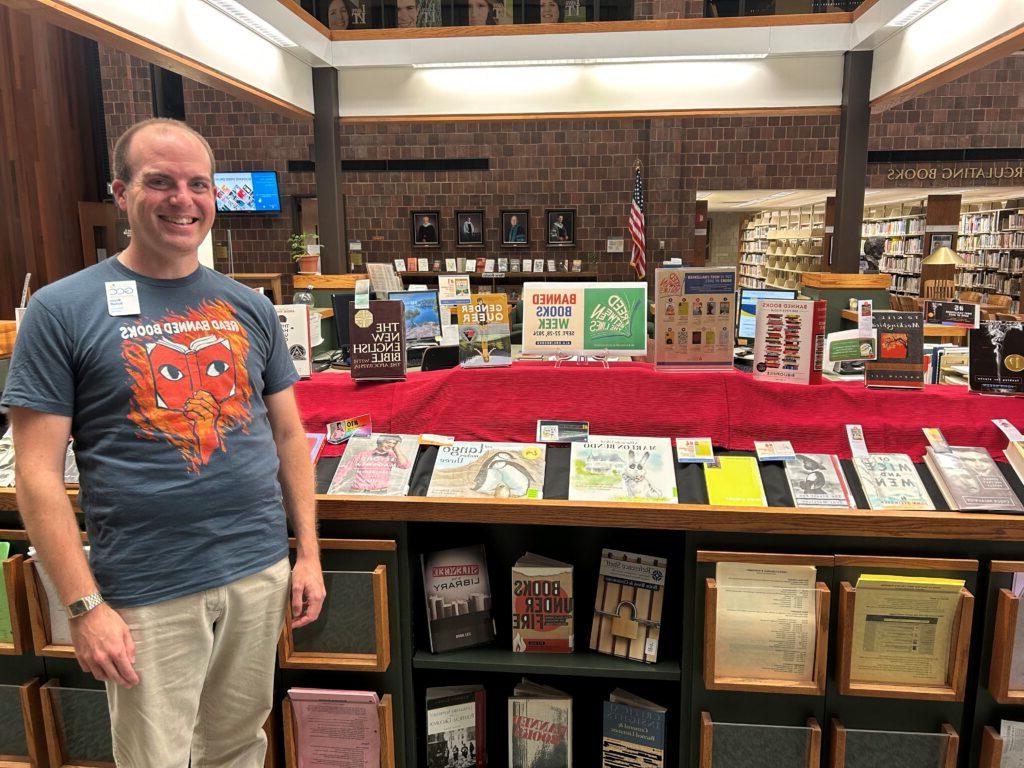 Banned book display in background with Part Time Reference Librarian Bryan Schuff in foreground wearing his Read Banned Books t-shirt